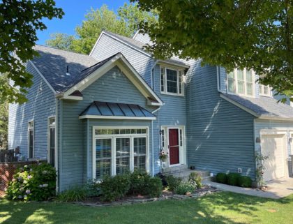Side view of blue two-story home with shingle and metal roofing, double-hung windows, three-car garage